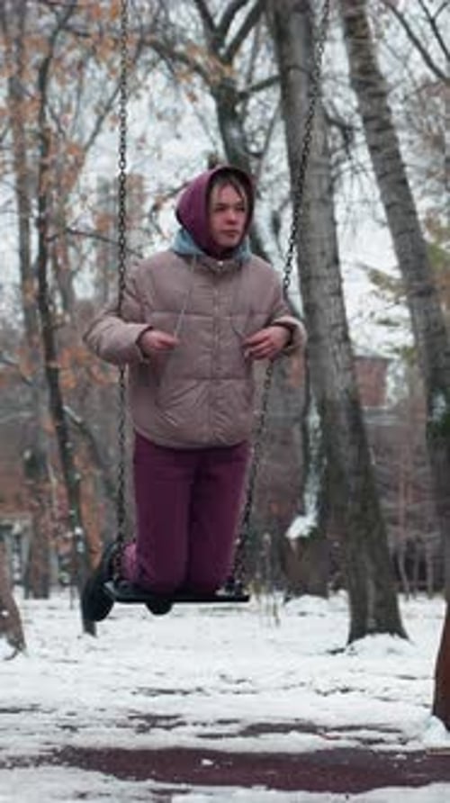 Lady Enjoying Swing on Snowy Winter Day in Playground with Trees in Background