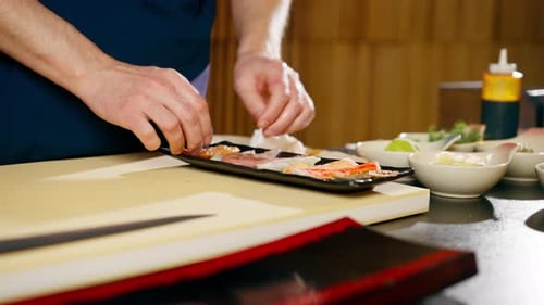 Closeup in Japanese Restaurant the Chef Lays Out Pieces of Raw Fish on a Plate