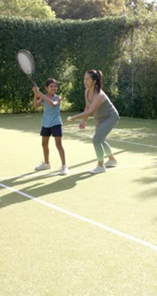 Vertical video: Playing tennis, girl hitting ball with racket while woman watches on court