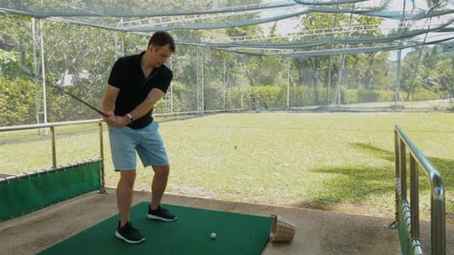 Man Practices Golf Swing on Tropical Driving Range
