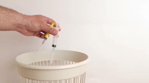 Hand Discards Syringes into Wastebasket for Safe Disposal