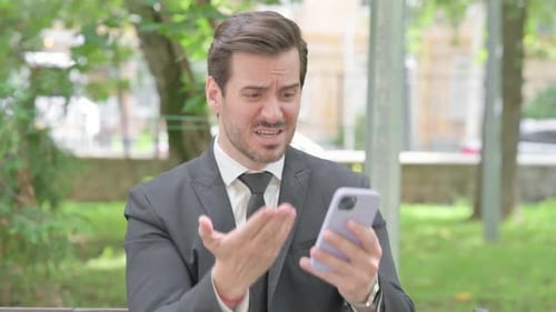 Upset Businessman Arguing on Smartphone in City Park