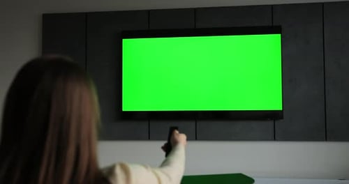 Woman Points Remote at Green Screen Television