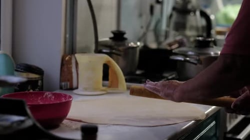 Hands Skillfully Rolling Dough with a Pin with Baking Supplies Around The Photo Emphasizes the