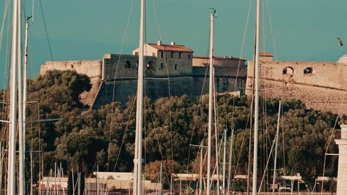 A historic stone fortress stands on a hill behind a dense marina full of sailboat masts