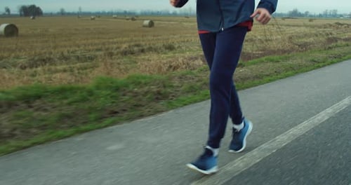 Close Up on Male Jogger Legs Running on a Road of a Countryside Field During Day. Motivated Mid
