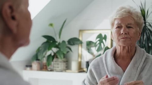 Senior Woman Examines Her Face in Mirror