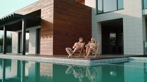 Beautiful Couple Drinking Cocktails Outside. Happy Couple Enjoying Sunbathing Near Swimming Pool