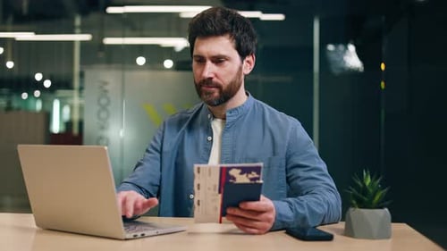 Male Keeping Flight Tickets in Hand While Typing on Pc and Smiling at Camera