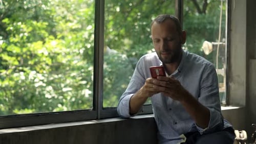 Young Man Using Smartphone Sitting by Window at Home Adult