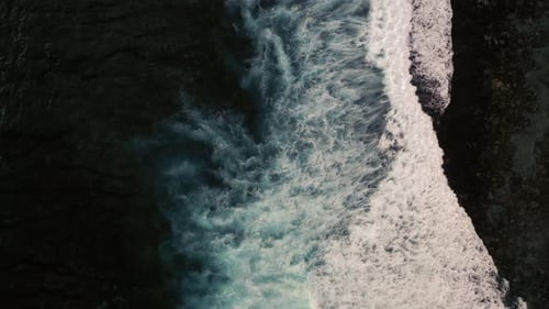 Aerial birds eye view of dramatic dark moody ocean water with white waves breaking