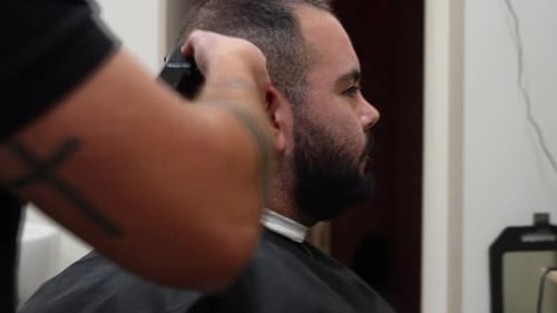 Profilaufnahme eines Mannes, der von einem tätowierten Friseur geschnitten wird