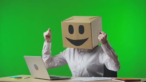 Frau in Pappschachtel mit lächelndem Emoji auf dem Kopf auf studiogrünem Hintergrund, den die Arbeiterin anschaut