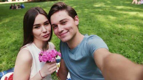 Attractive Young Couple in Love Sitting in the Park at Sunset Makes the Selfie Smartphone Camera