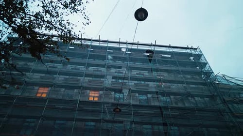 Un sitio de construcción bullicioso durante el anochecer con andamios y una imponente grúa que se cierne contra él
