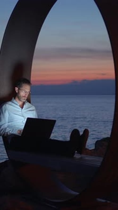 Man Working on Laptop by the Ocean at Sunset