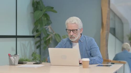 Senior Man Works On Laptop in Office