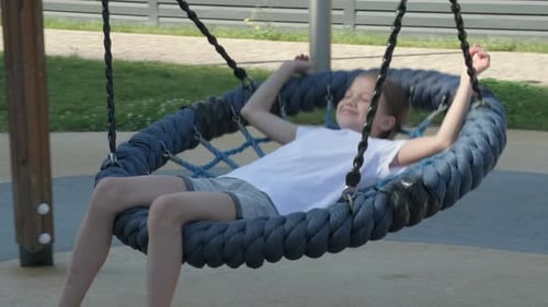 Kid Girl Smiling Swinging on Blue Round Swing in Playground on Summer Day
