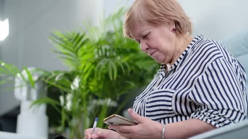 Woman Taking Notes While Looking at Cellphone