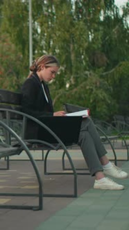 Businesswoman Reading Documents on Park Bench with Laptop in Peaceful Outdoor Setting