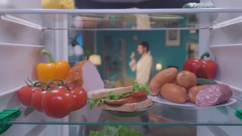 Refrigerator with Products on the Shelves Inside View The Door Opens a Man in a Bathrobe Stands