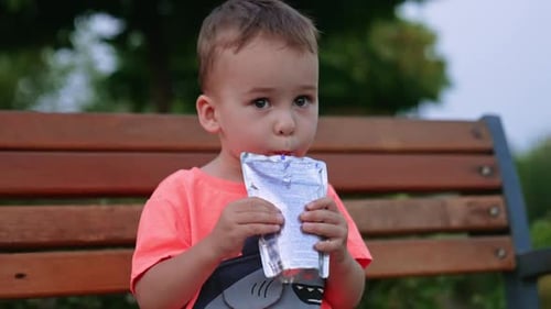 Un joli bambin caucasien aux yeux noirs est assis sur le banc à l'extérieur.