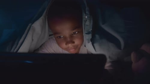 Garçon utilisant une tablette numérique sous une couverture dans une pièce sombre