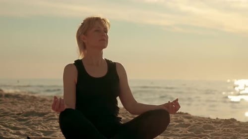 Slender Adult Woman Sitting on Yoga Mat in Lotus Position Outside Meditation at Sunset Beach