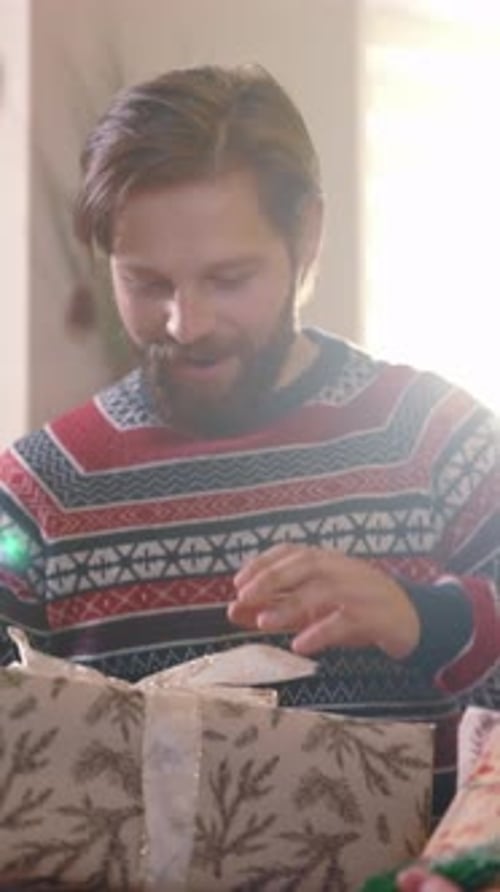 Man Smiling While Unwrapping a Christmas Present