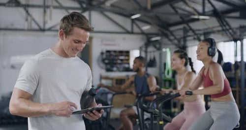Coach using a digital tablet in a gym while training a group fitness class
