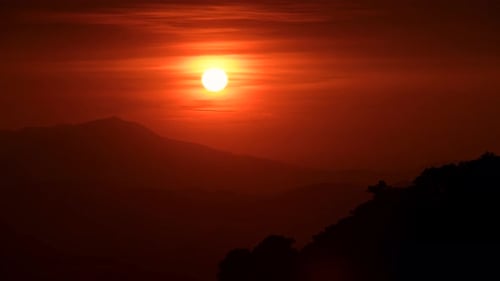 Der orangerote Sonnenuntergang wird von Wolken bedeckt, während er sich dem Horizont nähert.
