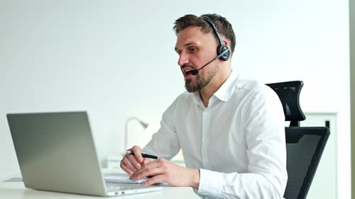 Businessman in Headset Working on Laptop During Video Conference in Office