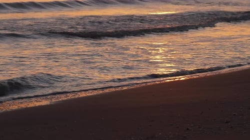 Sandstrand bei Sonnenaufgang mit Wellen, die an der Küste brechen und Sonnenlicht reflektieren, Mittelmeer, Clo