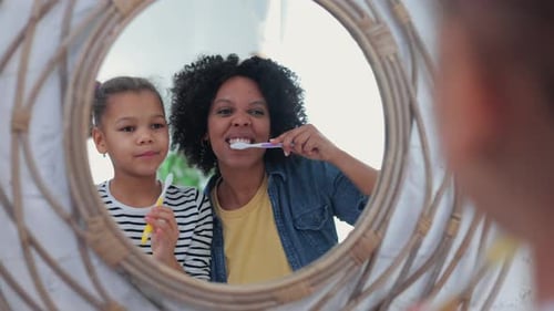 Woman and Child Brushing Teeth Together in Bathroom