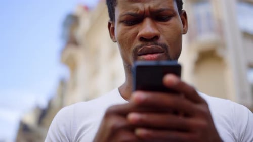 Focused african american man texting a message on an urban city street