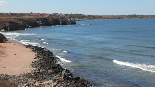 Shore with Grass and Hotels in the Distance Surrounded By the Black Sea Under a Clear Sky