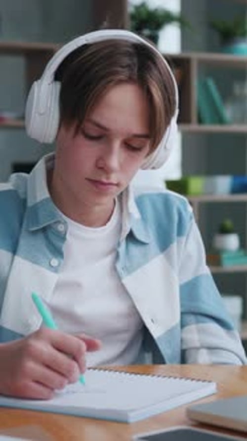 Teen Drawing in Notebook with Headphones at Desk