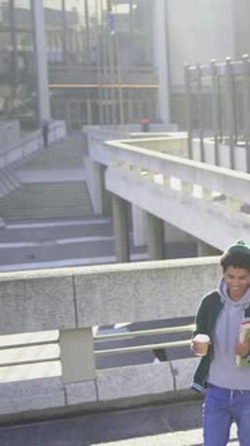 Vertical video: Walking student in beanie descending steps with coffee folders, heading to class