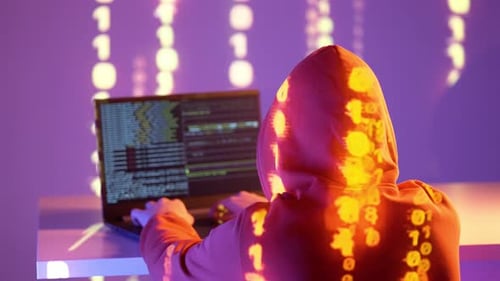 Orangefarbene Kapuzenfigur mit reflektiertem Binärcode beim Programmieren auf dem Laptop in einer neonbeleuchteten technischen Umgebung