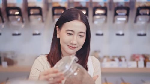 Young woman shopping at a zero waste store, holding a glass jar