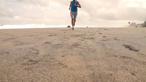 Young man jogging barefoot on a sandy beach in super slow motion