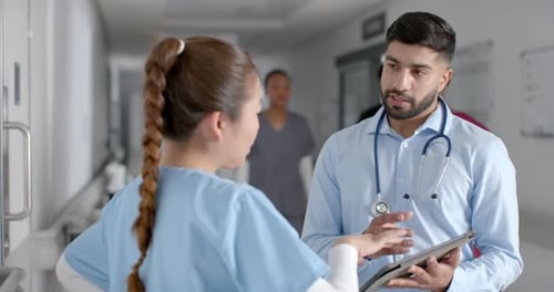 Diverse male and female doctors discussing work using tablet in hospital corridor, slow motion