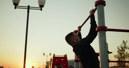 Young Athletic Man Works Out Doing Pullups on a Street Sports Ground at Sunset