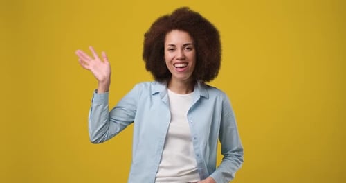 Junge lächelnde Afroamerikanerin, die Hand schüttelt, winkt und verabschiedet sich, während sie über dem Orange Studio steht