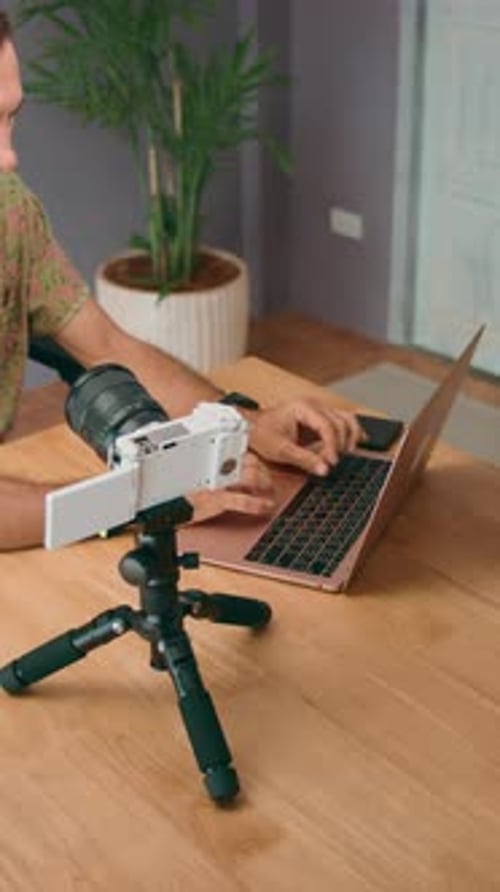A Vlogger is Seen Setting Up a Camera While Working on a Laptop at Their Home or Office Desk