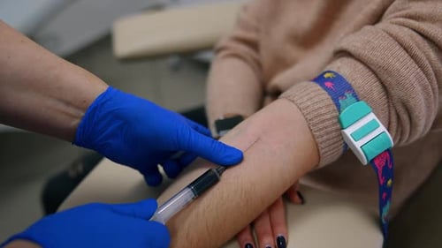 Medic’s hands in blue latex gloves fill the syringe with blood. Test sample taking from vein on arm.