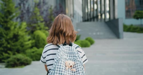 Little girl with backpack and textbook going hurrying to school. Attaractive schoolgirl
