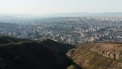 Aerial opening view of city of Tbilisi in Georgia appearing behind a mountain. Establishing shot, fo