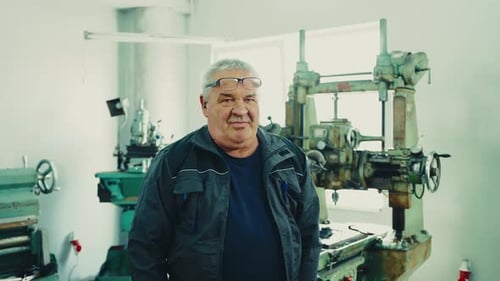 A portrait of an elderly engineer with raised glasses in a blue workshop in a workshop