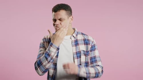 Jeune homme souffrant de maux de dents sur fond rose